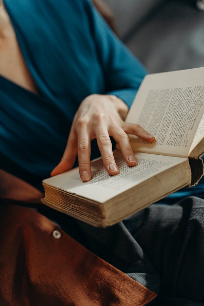 A detailed shot of a person reading a book, focusing on the hand turning a page indoors.