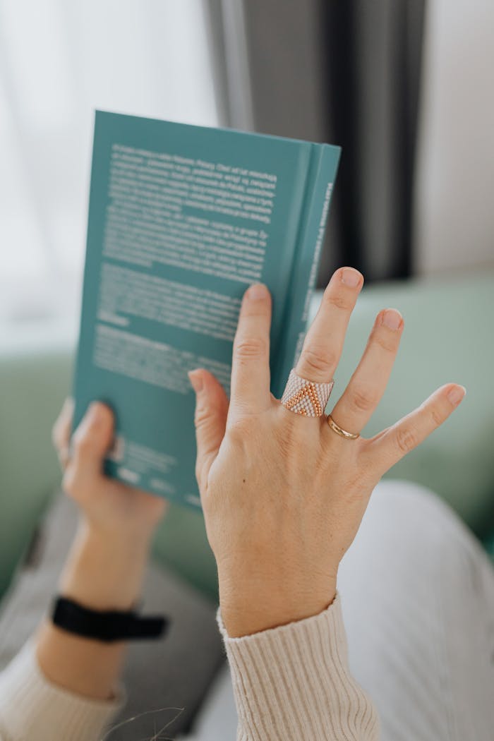 Hands holding a book, showcasing elegant rings in a cozy setting.